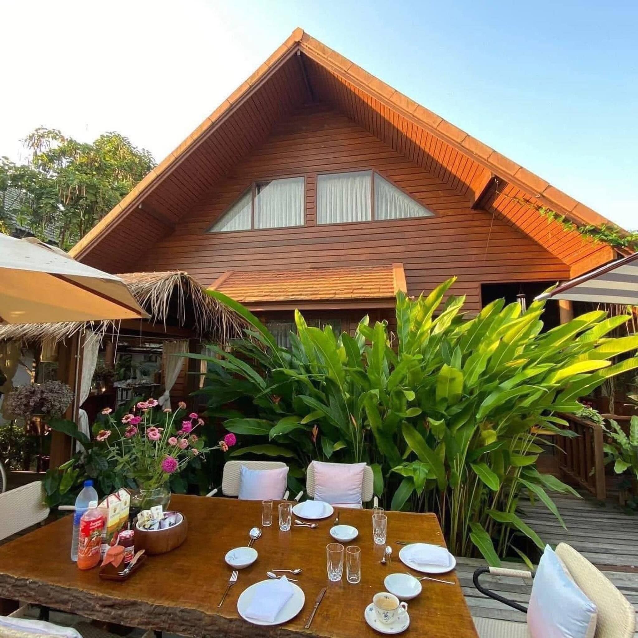 A wooden villa with a dining area set for two, featuring a table with plates, glasses, and a bottle.