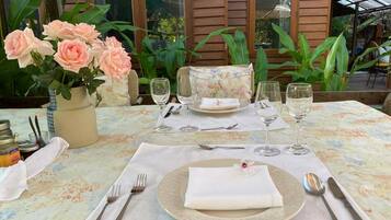 A table set for two with a floral tablecloth, a vase of pink roses, and a wicker basket.