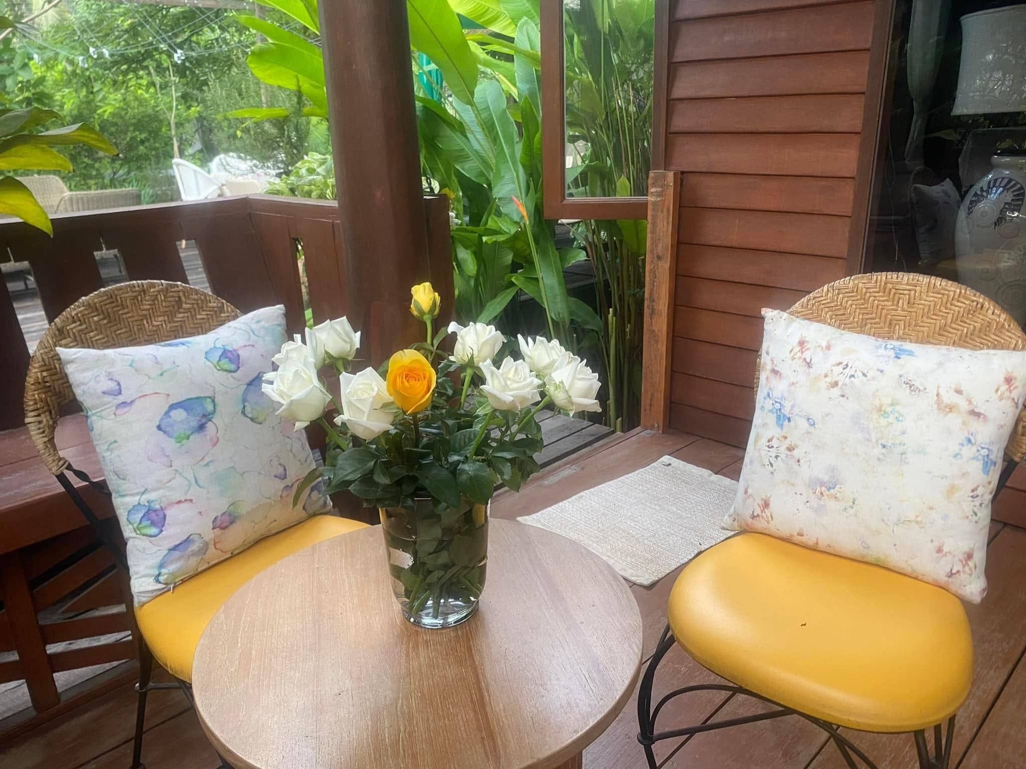 A wooden deck with two wicker chairs, a small round table, and a vase with flowers.