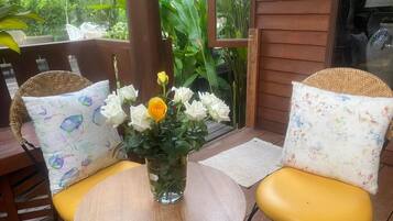 A wooden deck with two wicker chairs, a small round table, and a vase with flowers.