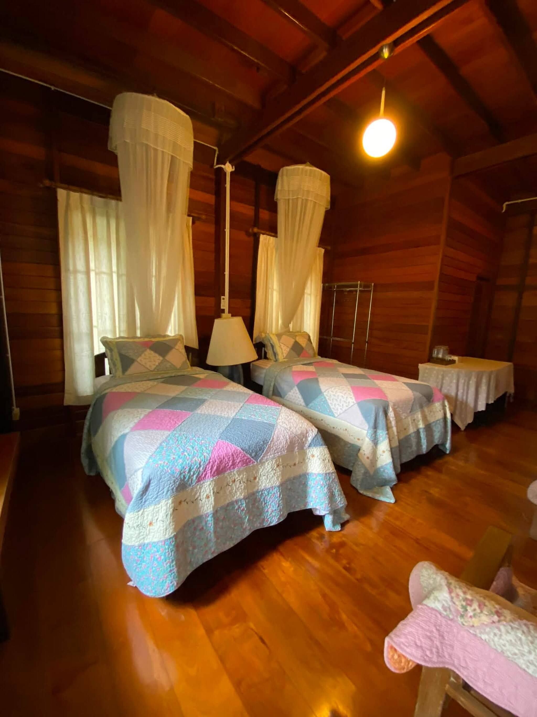 A room with two beds, wooden floors, and a hanging light fixture.