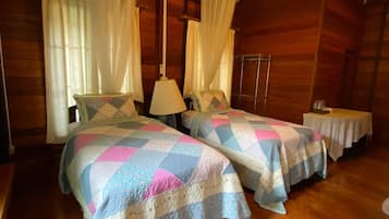 A room with two beds, wooden floors, and a hanging light fixture.