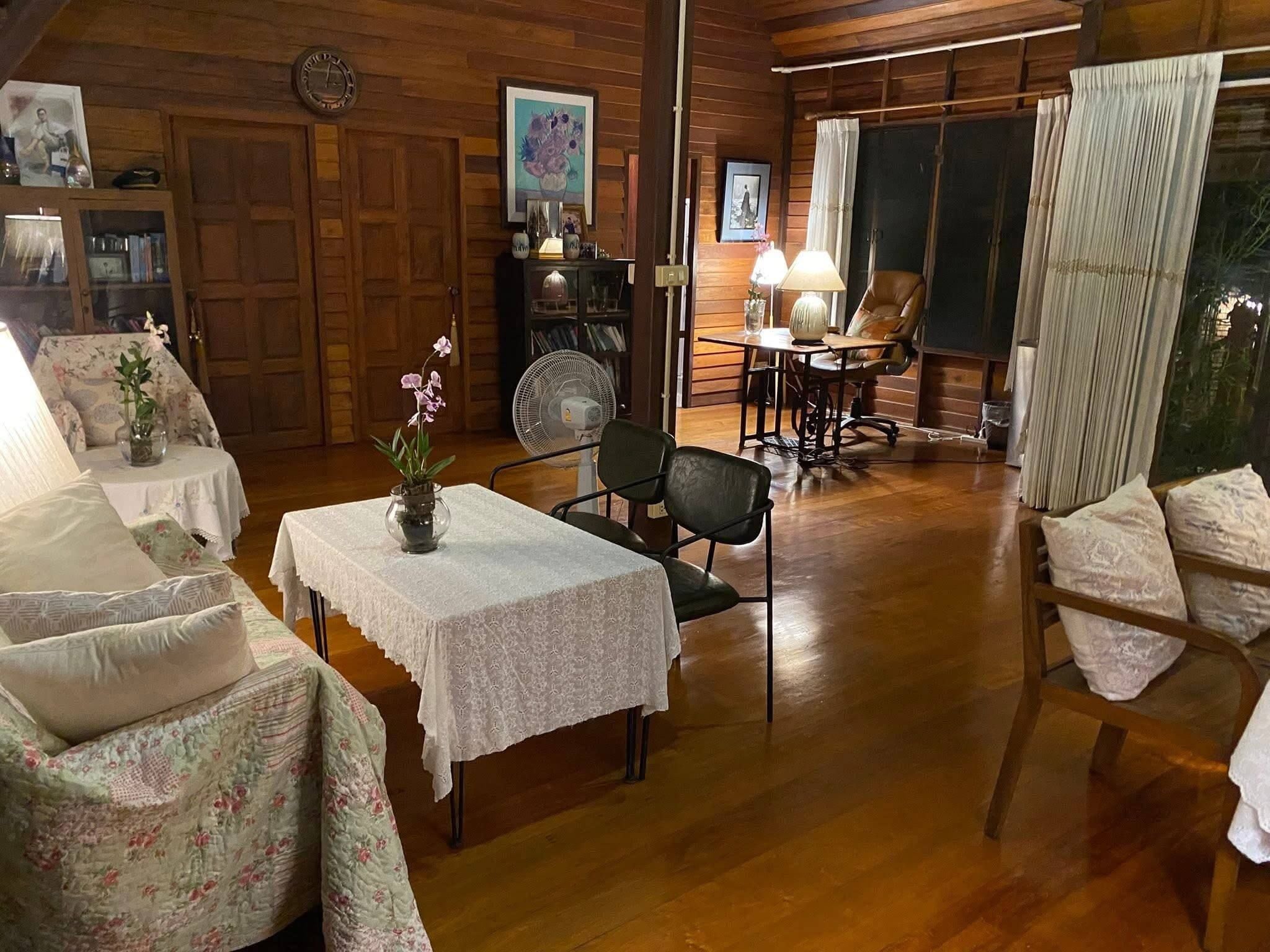 A cozy room with wooden walls, a dining table with chairs, a fan, and a window with curtains.