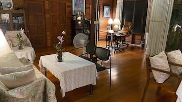 A cozy room with wooden walls, a dining table with chairs, a fan, and a window with curtains.