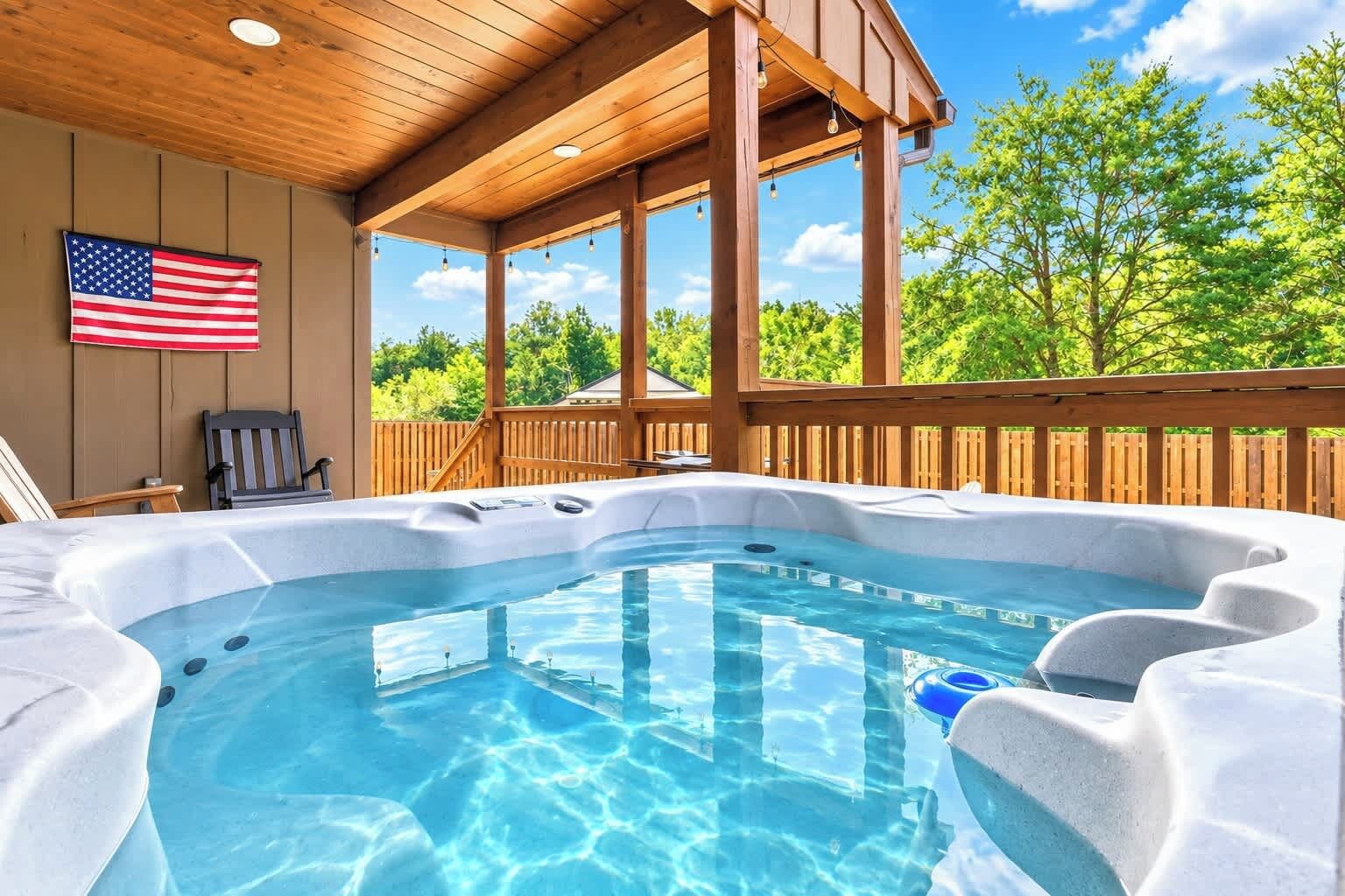 Un bain à remous avec une terrasse en bois, un drapeau américain et un ciel bleu clair en arrière-plan.