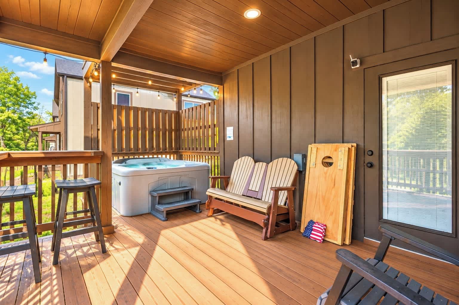 A covered deck with a hot tub, wooden chairs, and a wooden bench.