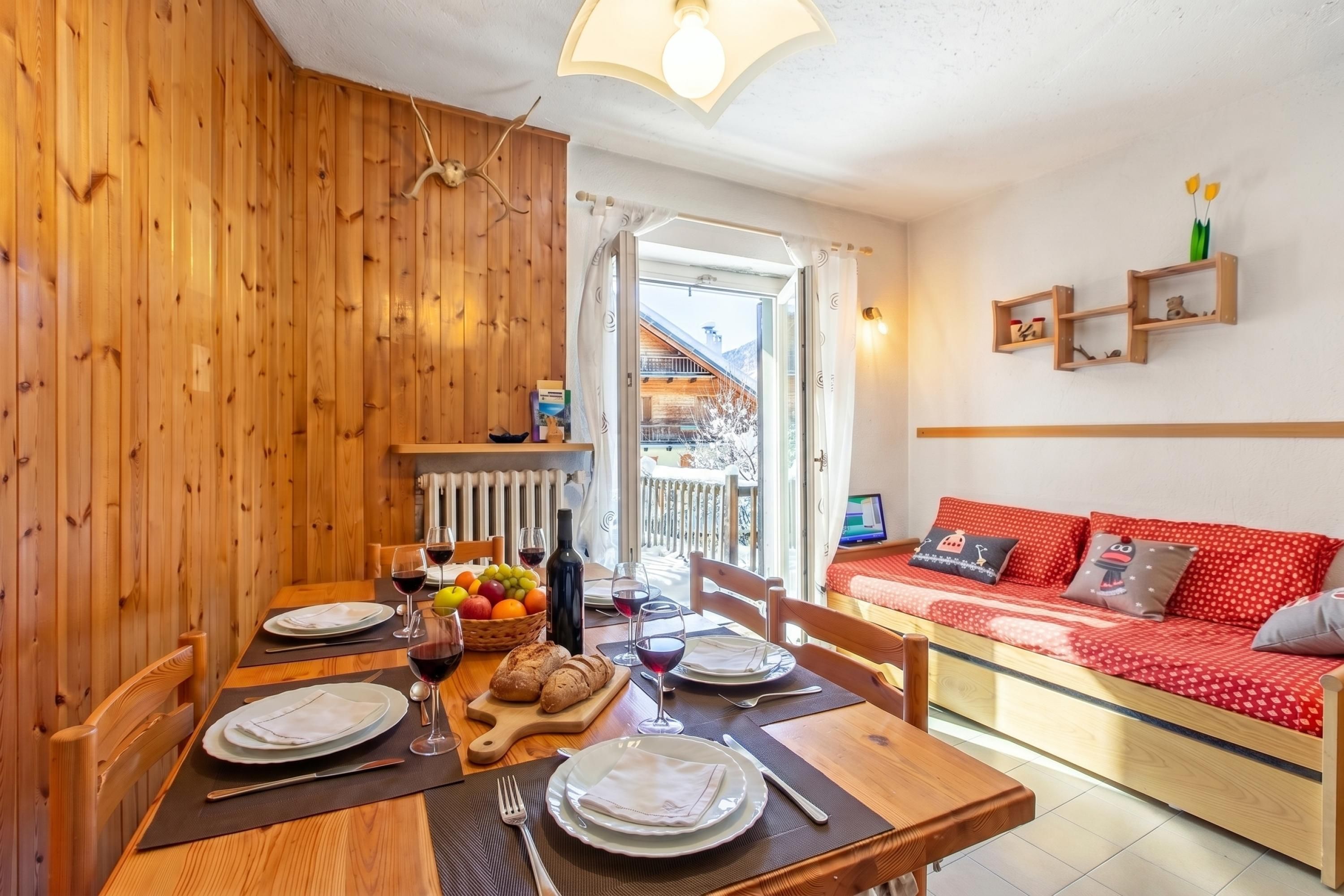 A dining area with a wooden table set for two, a red sofa, and a view of a mountain in the background.