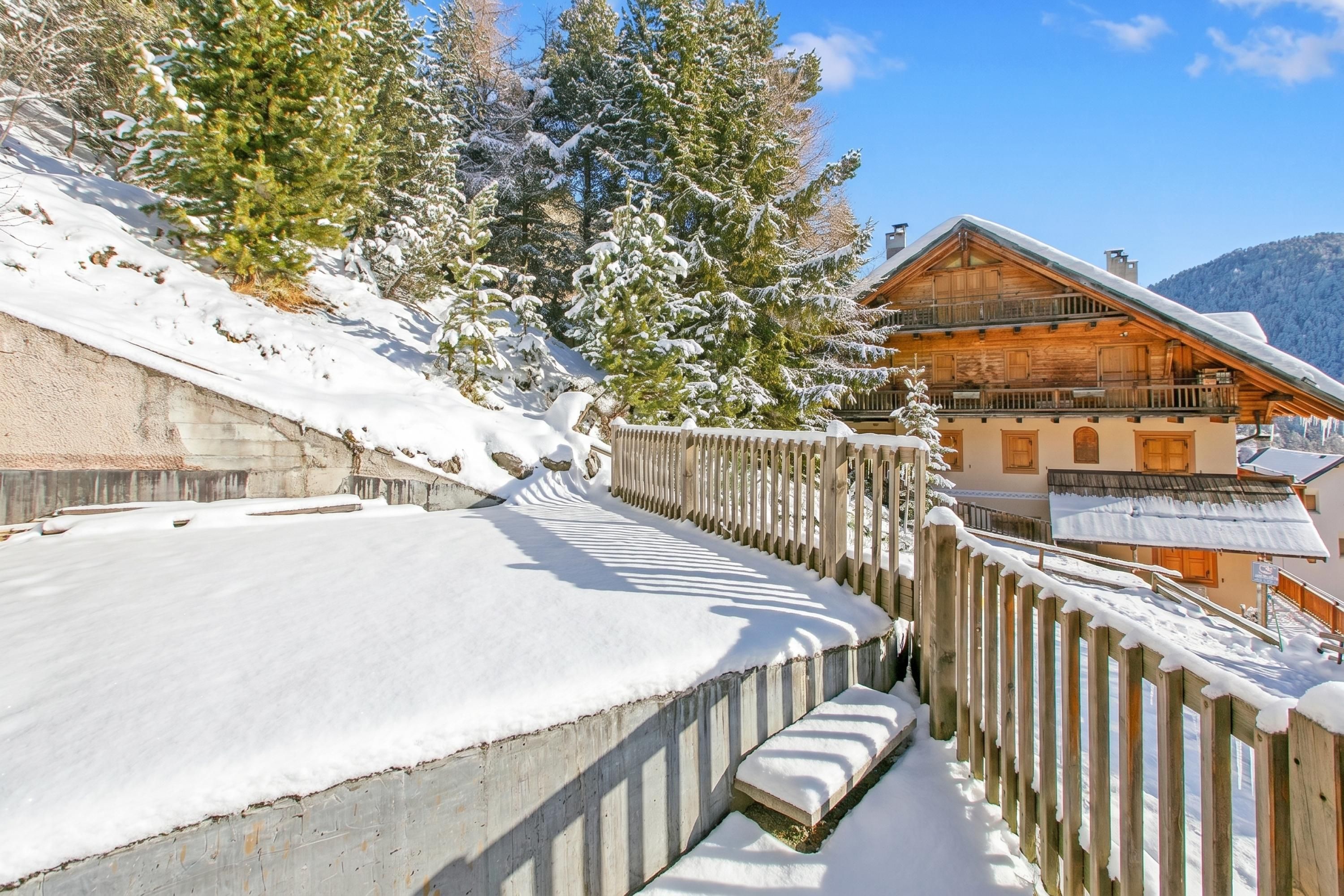 A wooden chalet with a snow-covered roof, a wooden fence, and a snow-covered slope.