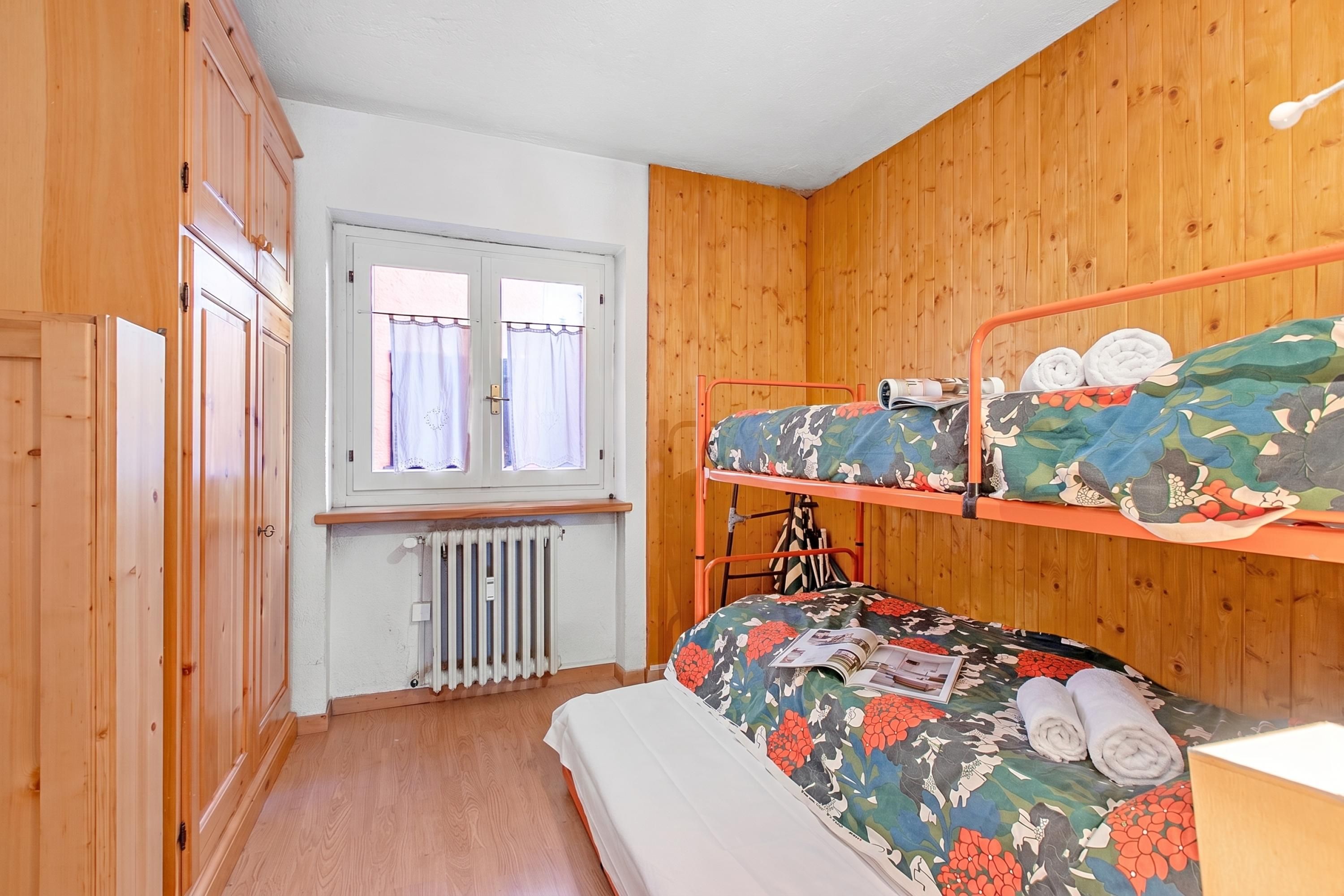 Habitación con literas, paredes de madera, una ventana con cortinas y un radiador.