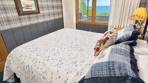Een slaapkamer met een groot bed, een raam met gordijnen, een ingelijste foto aan de muur en een lampje op het nachtkastje.