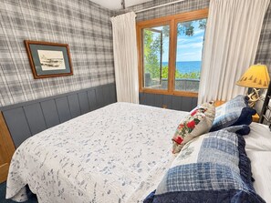 Une chambre avec un grand lit, une fenêtre avec des rideaux, un tableau encadré au mur et une lampe sur la table de chevet.