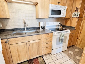 A kitchen with wooden cabinets, a stainless steel sink, a white microwave, and a stove.
