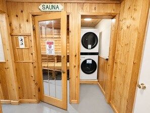 A sauna room with wooden walls and a glass door, featuring a sign that reads 'SAUNA' and a warning sign about water on the floor.