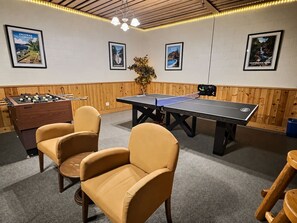 A room with a foosball table, ping pong table, and two chairs.