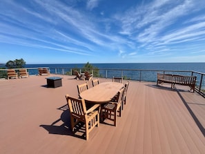 Une terrasse en bois avec une table ronde et des chaises, donnant sur une étendue d’eau.