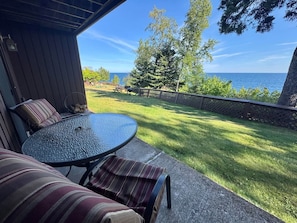 An outdoor patio with a round table and striped cushions, overlooking a grassy area and a body of water.