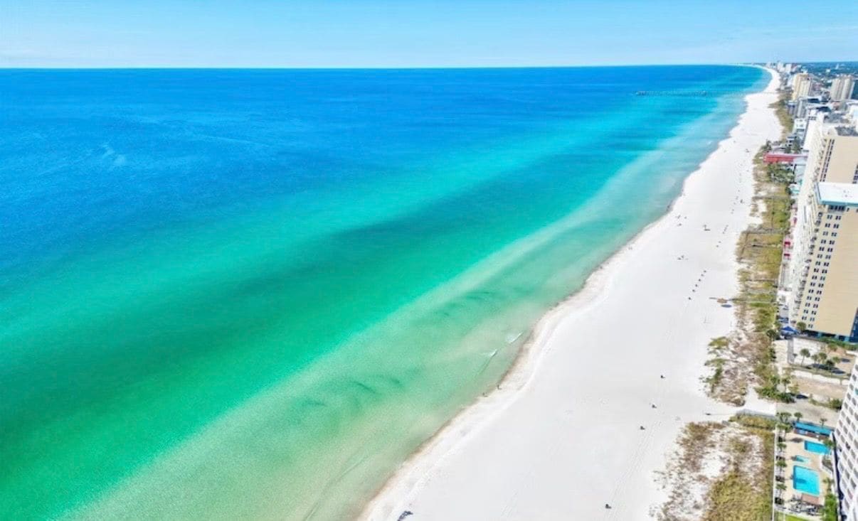 An aerial view of a beach with clear turquoise water and a sandy shore.