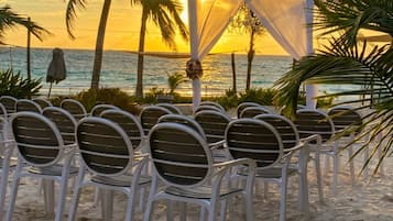 Een stranddecor met een witte luifel en stoelen, ingericht voor een evenement.
