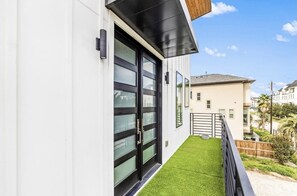 A modern building with a balcony, a black-framed door, and a small grassy area. - Modern/Luxury/Rooftop Deck/Downtown/Heated Pool/5BDRM (Houston)