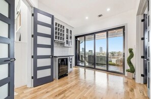 A modern interior with a sliding glass door leading to a balcony, a built-in kitchen area, and a wooden floor. - Modern/Luxury/Rooftop Deck/Downtown/Heated Pool/5BDRM (Houston)