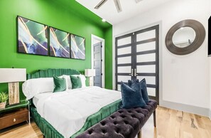 A bedroom with a green wall, a bed with white and green bedding, a bench, a round mirror, and a door with a black frame. - Modern/Luxury/Rooftop Deck/Downtown/Heated Pool/5BDRM (Houston)