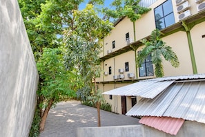 Um pátio com um caminho, um edifício com várias janelas e aparelhos de ar condicionado, e uma palmeira.
