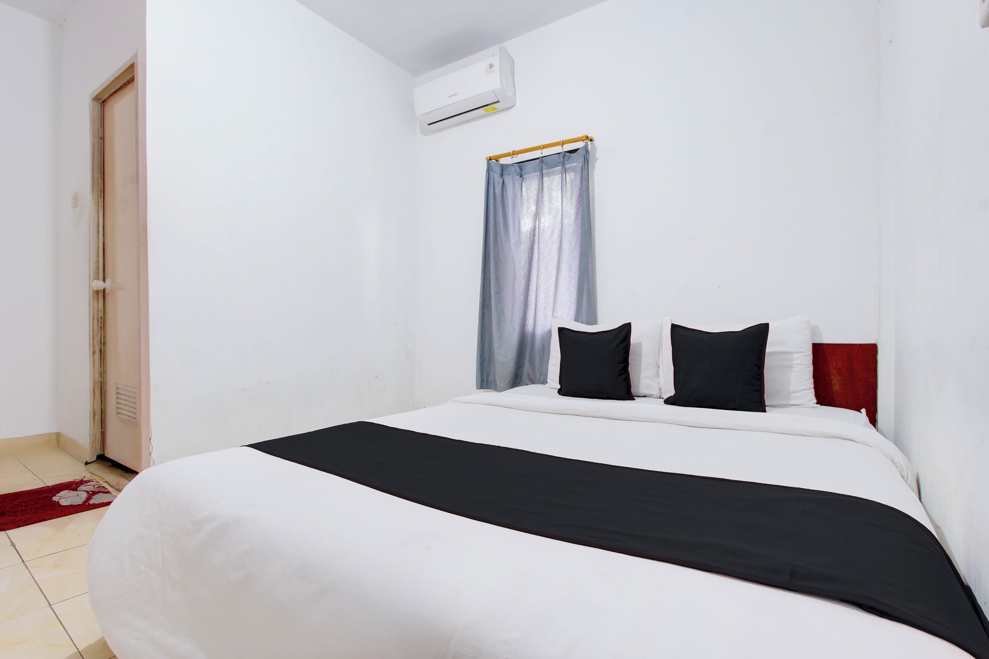 A hotel room with a bed, a window with a curtain, an air conditioning unit, and a door.