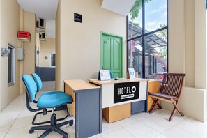 A hotel reception desk with a sign indicating it is company-serviced, a green door labeled 'Office', and a view of the outside through large windows. - Hotel O near Ahmad Yani International  (Semarang)