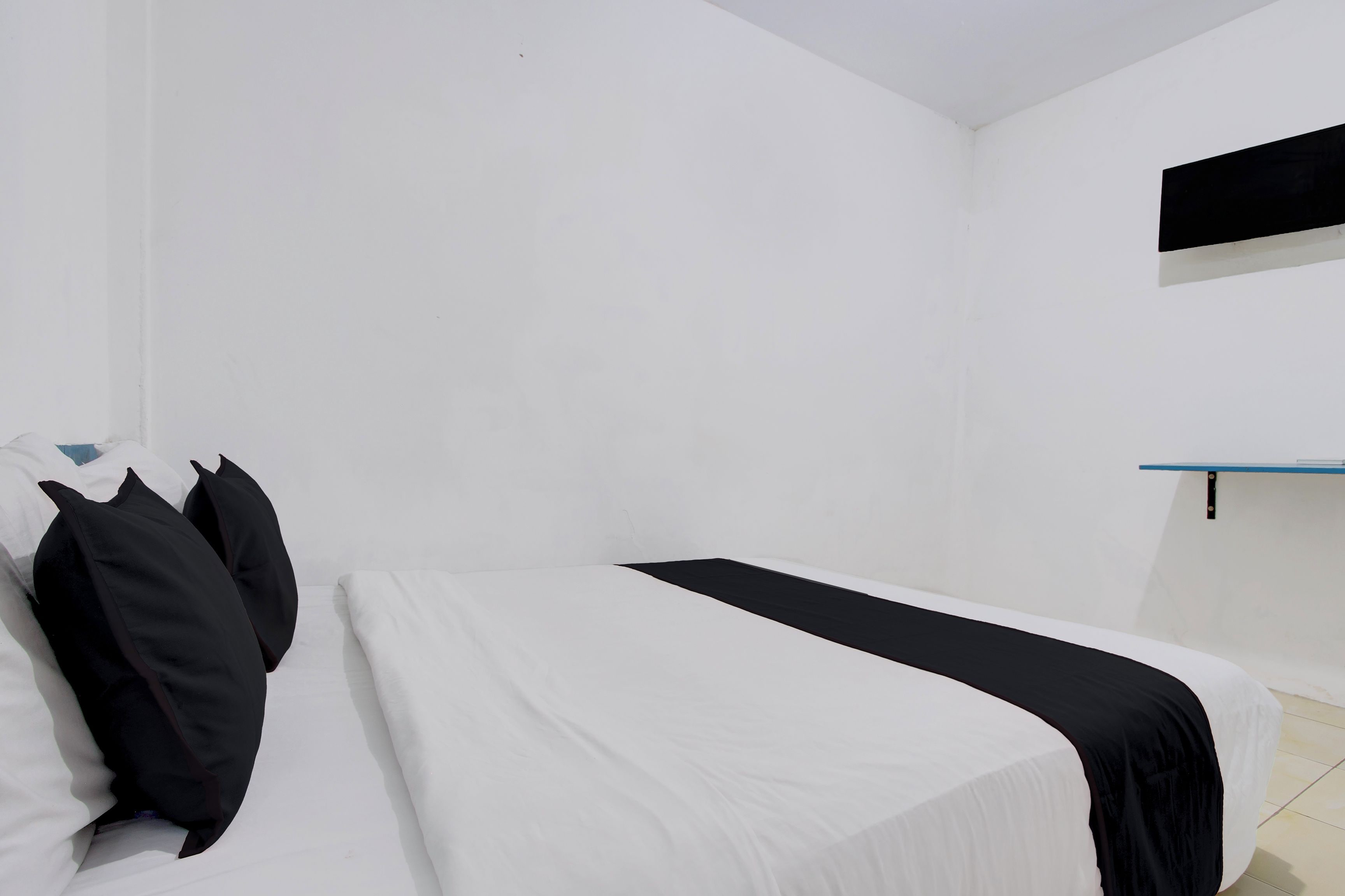 Una habitación sencilla y despejada, con cama, almohadas y una repisa.