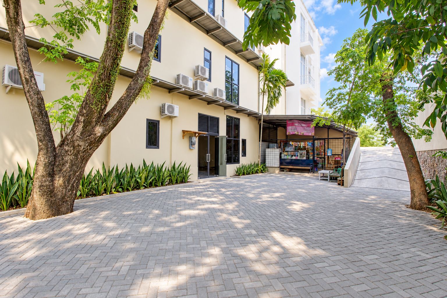 Un edificio con un patio empedrado, unidades de aire acondicionado y una pequeña zona de estar al aire libre.