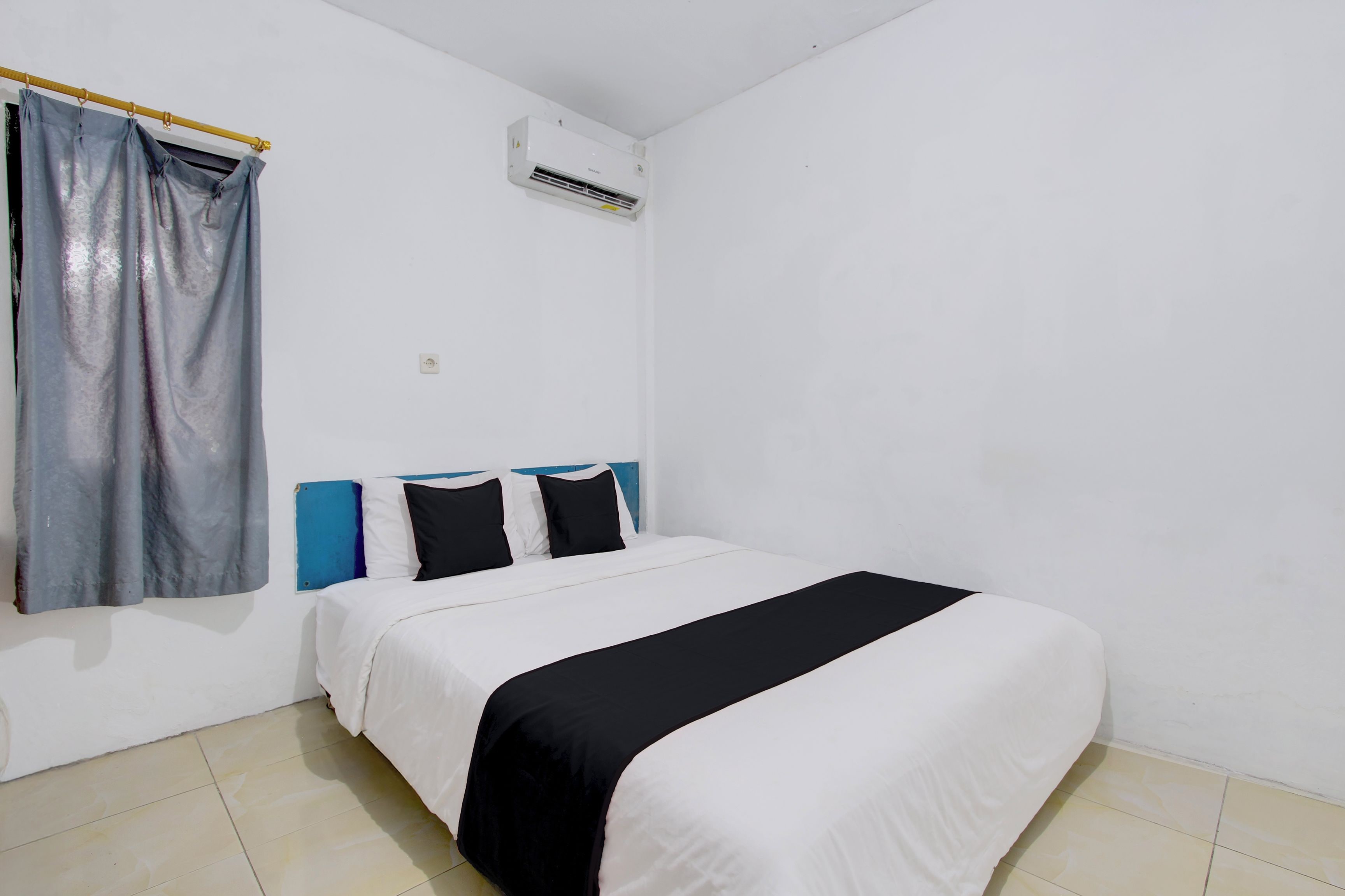 Una habitación sencilla y limpia con cama, cortina y equipo de aire acondicionado.