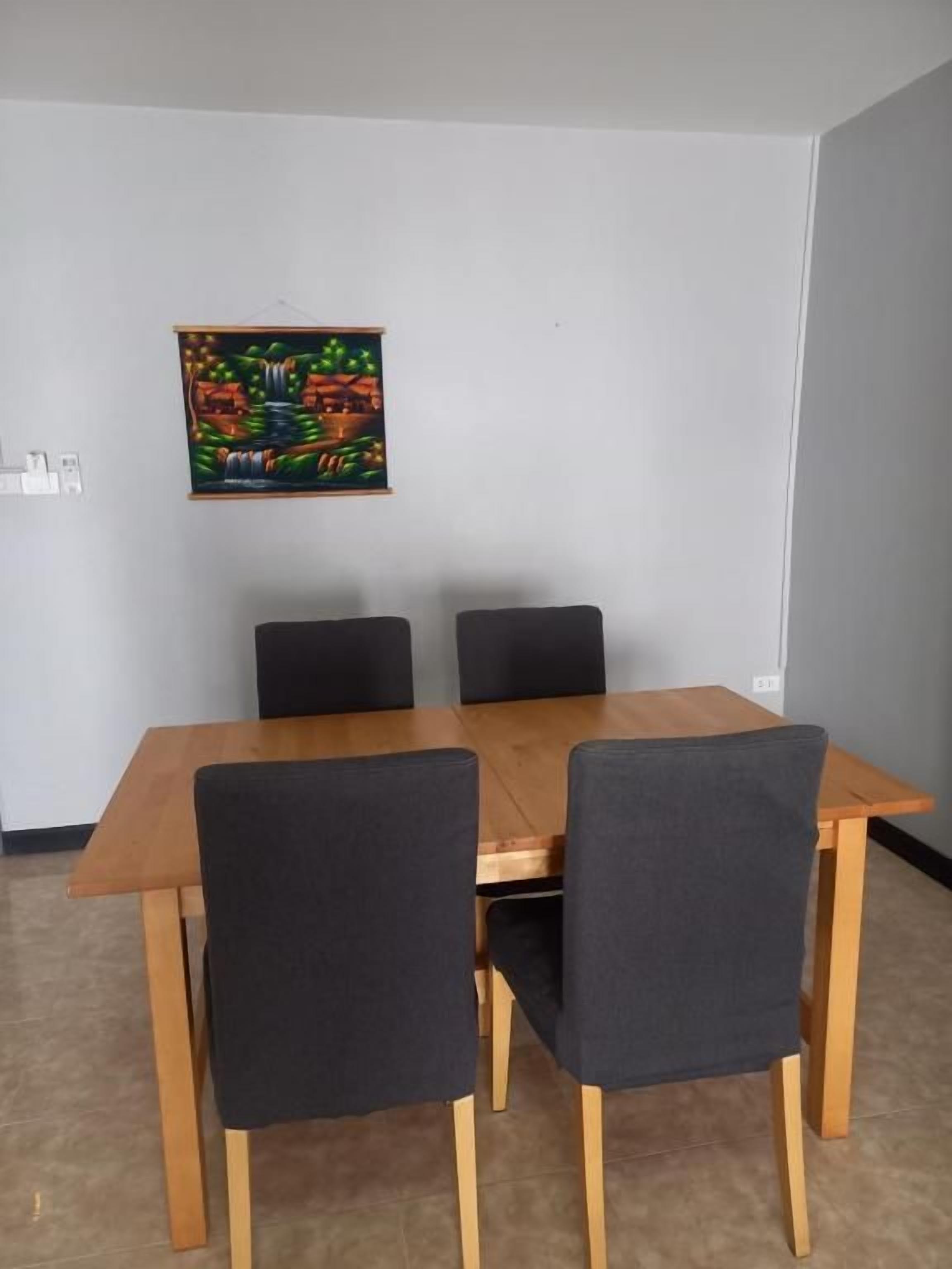 A dining area with a wooden table and four chairs, a painting on the wall, and a light switch.