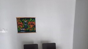 A dining area with a wooden table and four chairs, a wall-mounted painting, and a light switch. - Dania Pattaya (Pattaya)