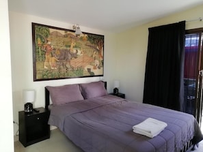 Ein Schlafzimmer mit einem Bett, zwei Nachttischen, einem Wandbild und einem Fenster mit Vorhängen.