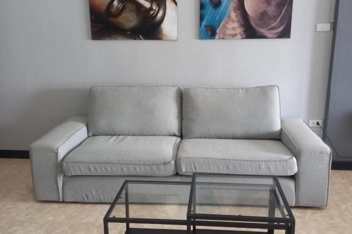Ein Wohnzimmer mit einem grauen Sofa, einem Glastisch und zwei Buddha-Gemälden an der Wand.