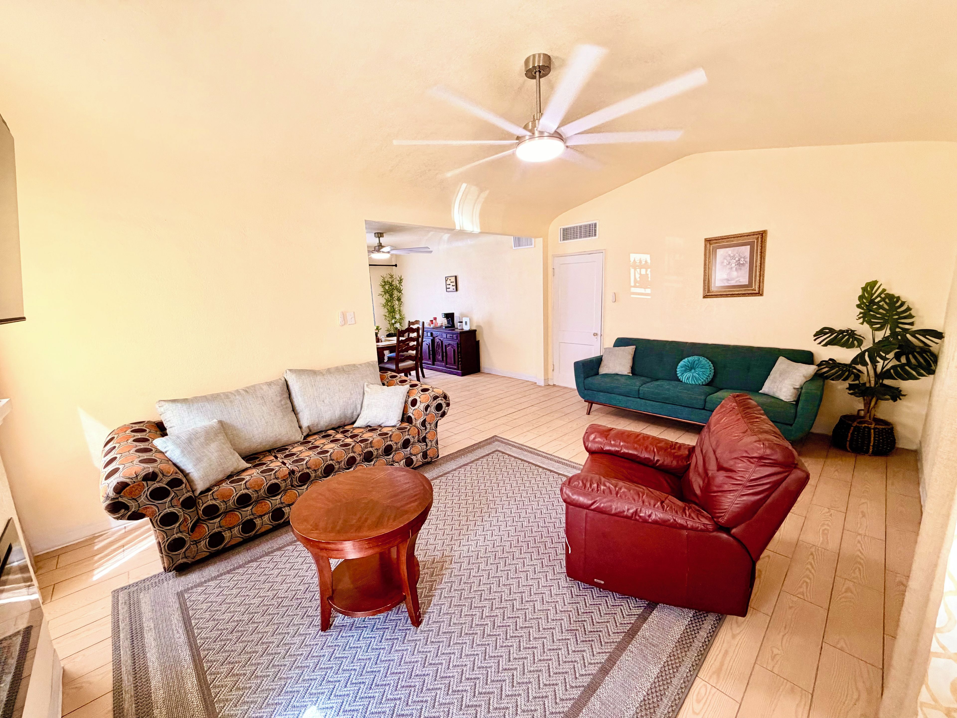 A living room with a patterned sofa, a red leather chair, a wooden coffee table, and a ceiling fan.