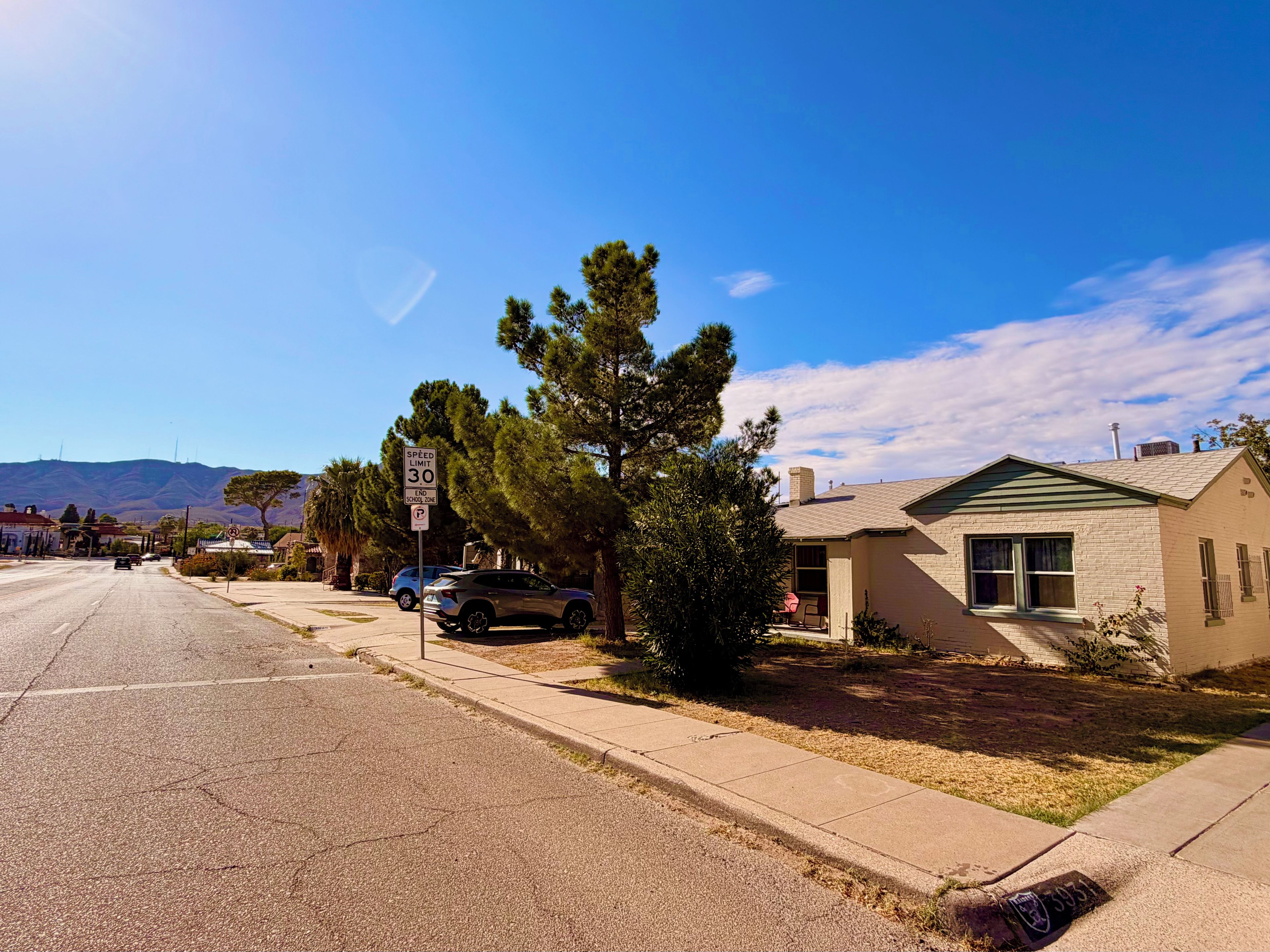 A residential street with houses, a speed limit sign, and a clear sky.