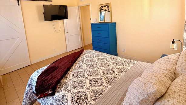 A bedroom with a bed, a ceiling fan, a TV mounted on the wall, a blue dresser, and a door.