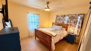 A bedroom with a bed, a ceiling fan, a dresser, and a nightstand.
