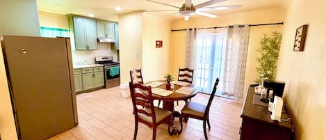 A compact kitchen with a dining area, a ceiling fan, and a refrigerator.