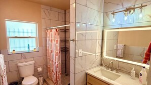 A bathroom with a toilet, sink, mirror, and shower area.