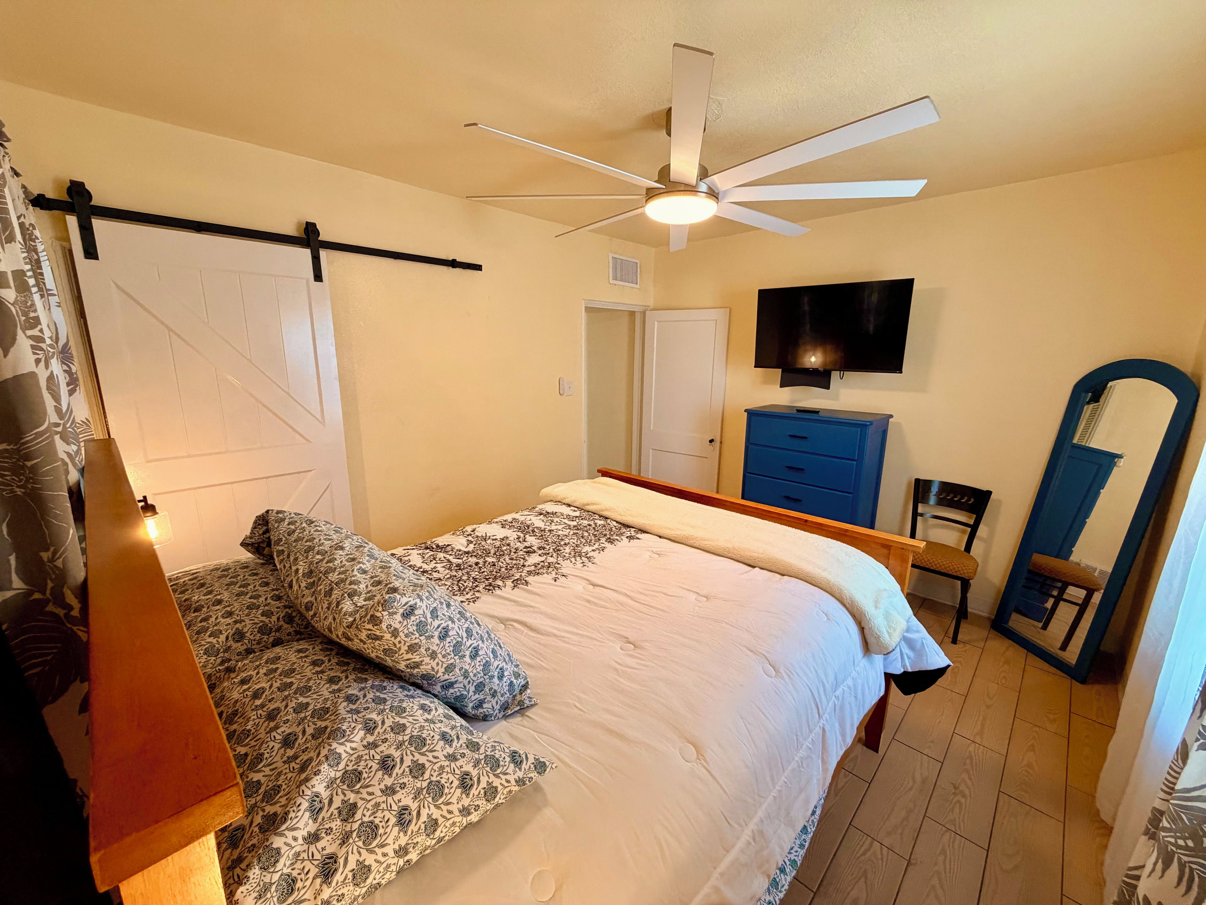 A bedroom with a bed, a ceiling fan, a TV, a dresser, and a mirror.
