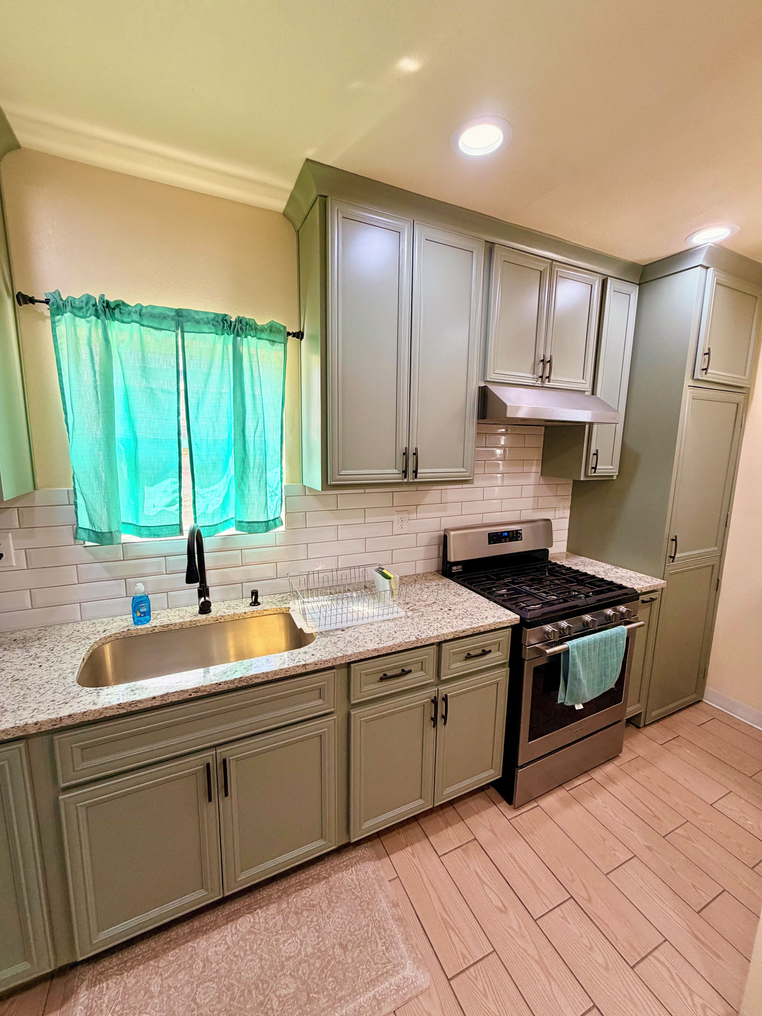 A kitchen with a stainless steel sink, a stove, and light green cabinets.