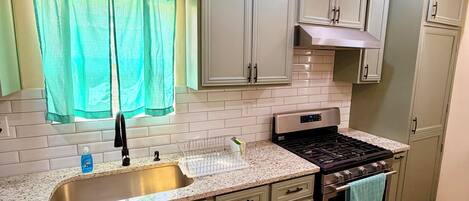 Una cocina con un lavamanos de acero inoxidable, una estufa y armarios verde claro.