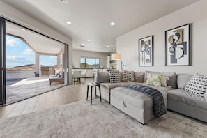 A spacious living area with a large sofa, a coffee table, and a view of the outdoors. - The Mountain Watch | Infinity Pool & Casita (Fountain Hills)