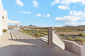 Un balcon en béton avec une rambarde en métal, donnant sur un paysage désertique avec des montagnes à l’horizon.