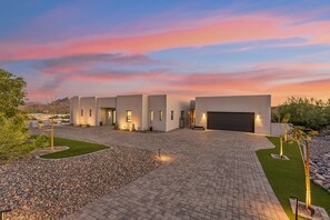 Une maison moderne dotée d’une allée pavée, d’un garage et d’espaces aménagés avec des arbres et des arbustes.