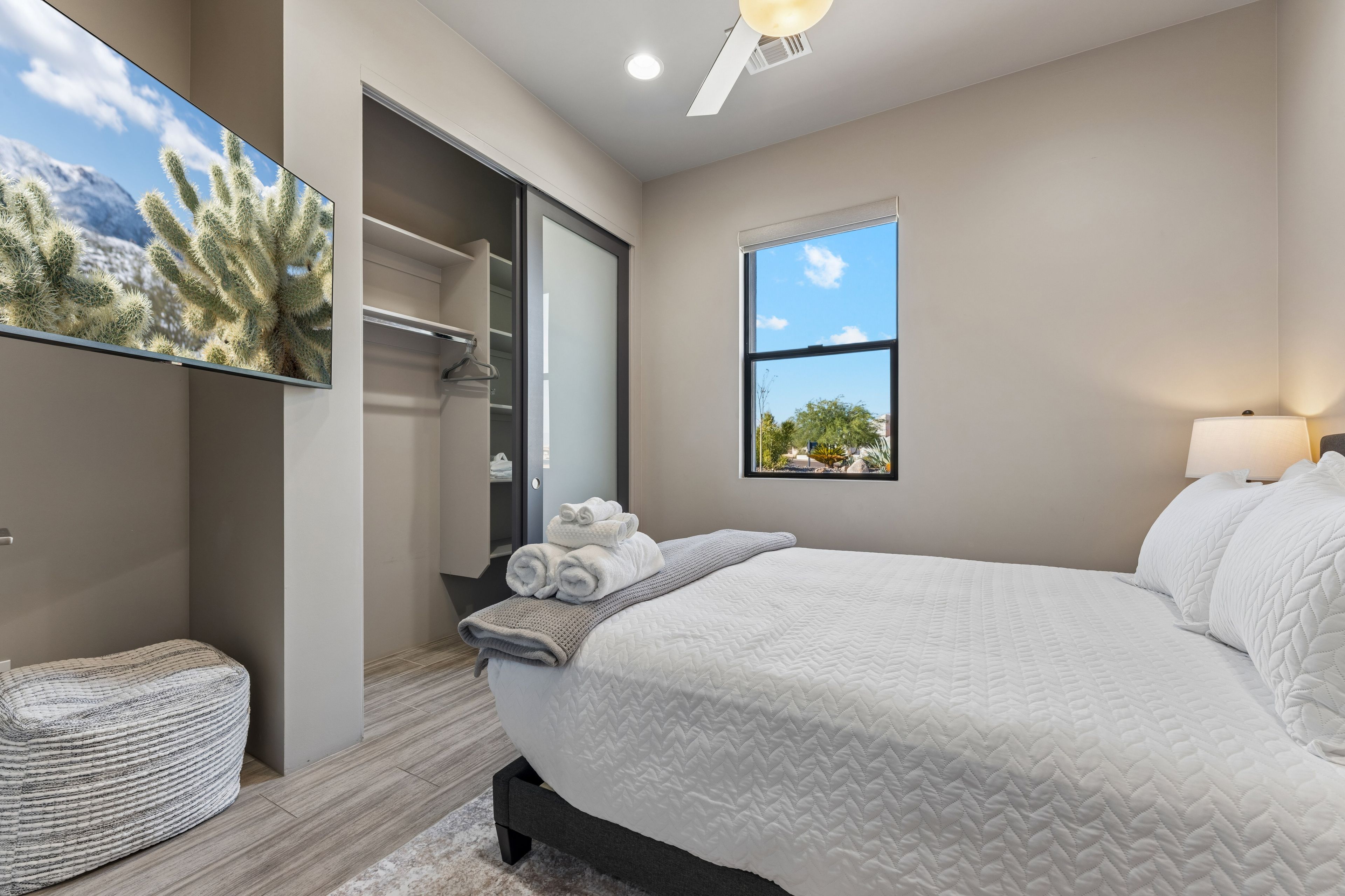 A bedroom with a bed, a window, a closet, and a wall-mounted TV.