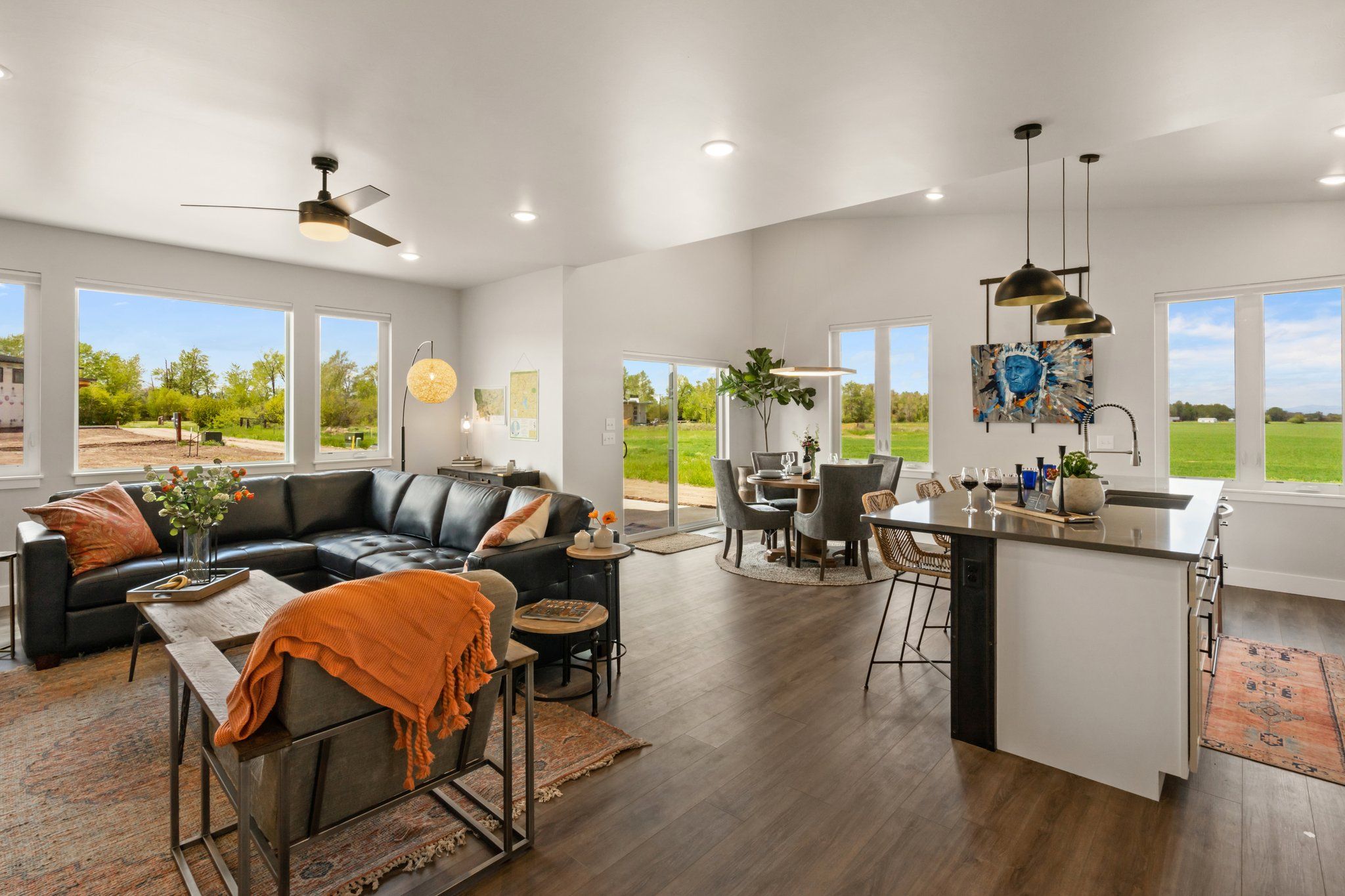 A spacious living area with a black leather sofa, a dining table, and a kitchen island with a sink.
