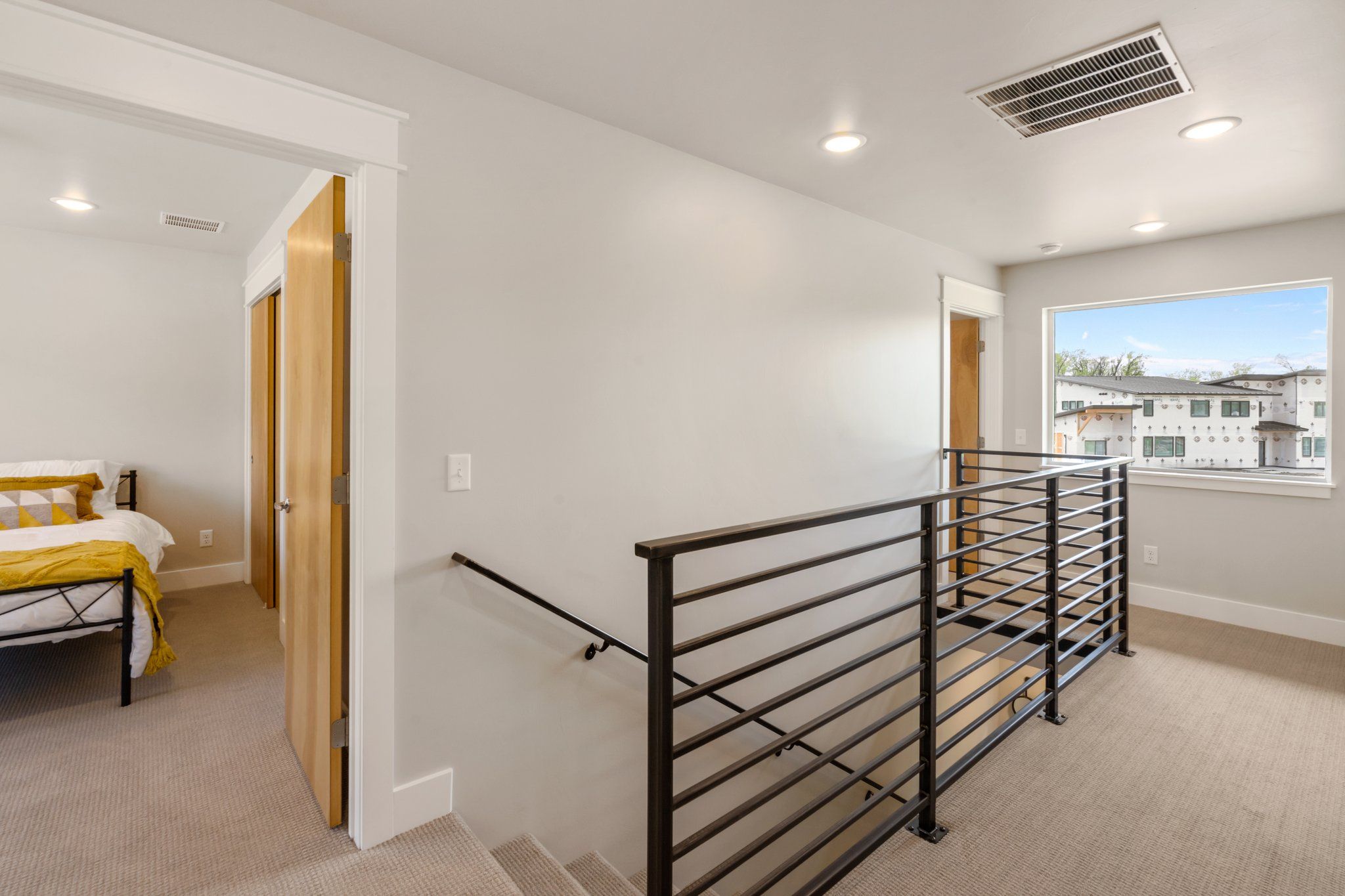 A bedroom with a bed, a wooden door, a window, and a staircase with a metal railing.